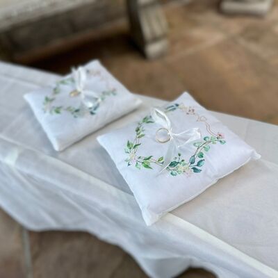 Bild vergr&ouml;&szlig;ern: Auf dem Bild sind zwei Ringkissen auf einem Tisch liegend zu sehen. Die Ringkissen haben eine grüne Ornamentstickerei. Mittig vom Kissen sind die Eheringe an weißen Bändern angebunden.